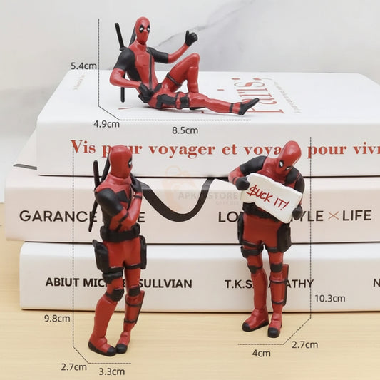 Deadpool action figure shown in two poses with overlaid dimension lines and measurements, placed in front of stacked white books. The product is the figurine itself, not the books or the store watermark.